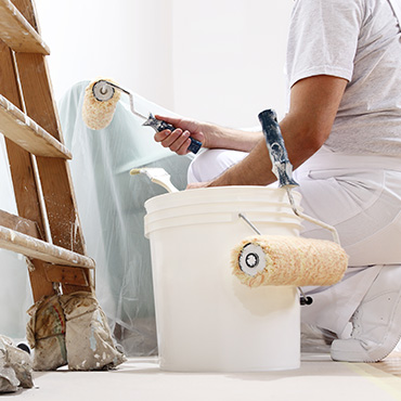 Gros plan sur un artisan qui peint un mur avec un peau de peinture blanc et une échelle