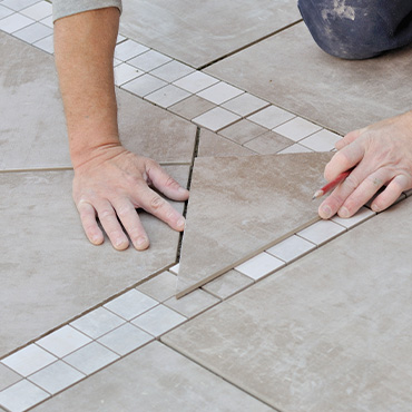 Gros plan sur un artisan qui pose du carrelage gris au sol