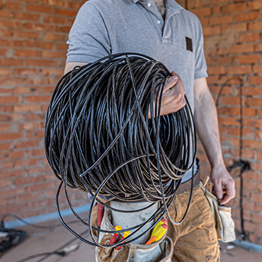 Photo d'un électricien qui porte un rouleau de câble noir